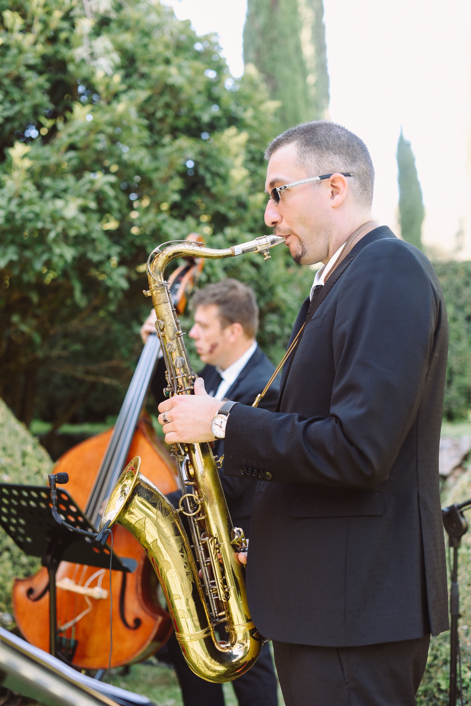 Saxophonist playing in a garden with a double bass player behind him at a wedding near Siena