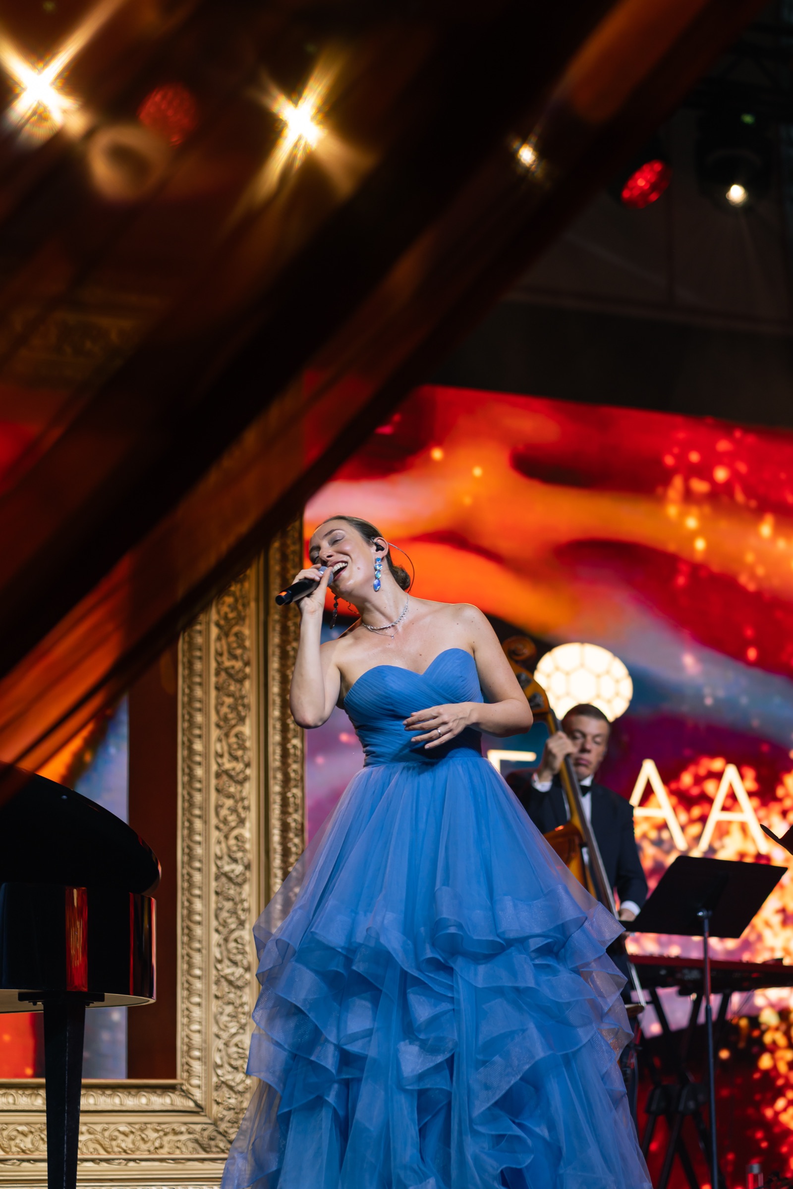 Italian jazz band vocalist in a blue gown on stage beside a double bass, with gilded frames behind, at a private island in the Maldives