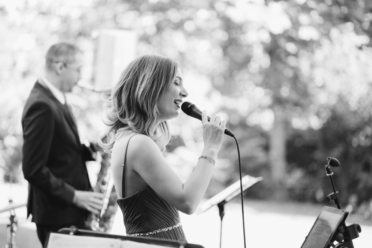 Black and white photo of the vocalist singing outdoors with the saxophonist behind her at a wedding in Tuscany
