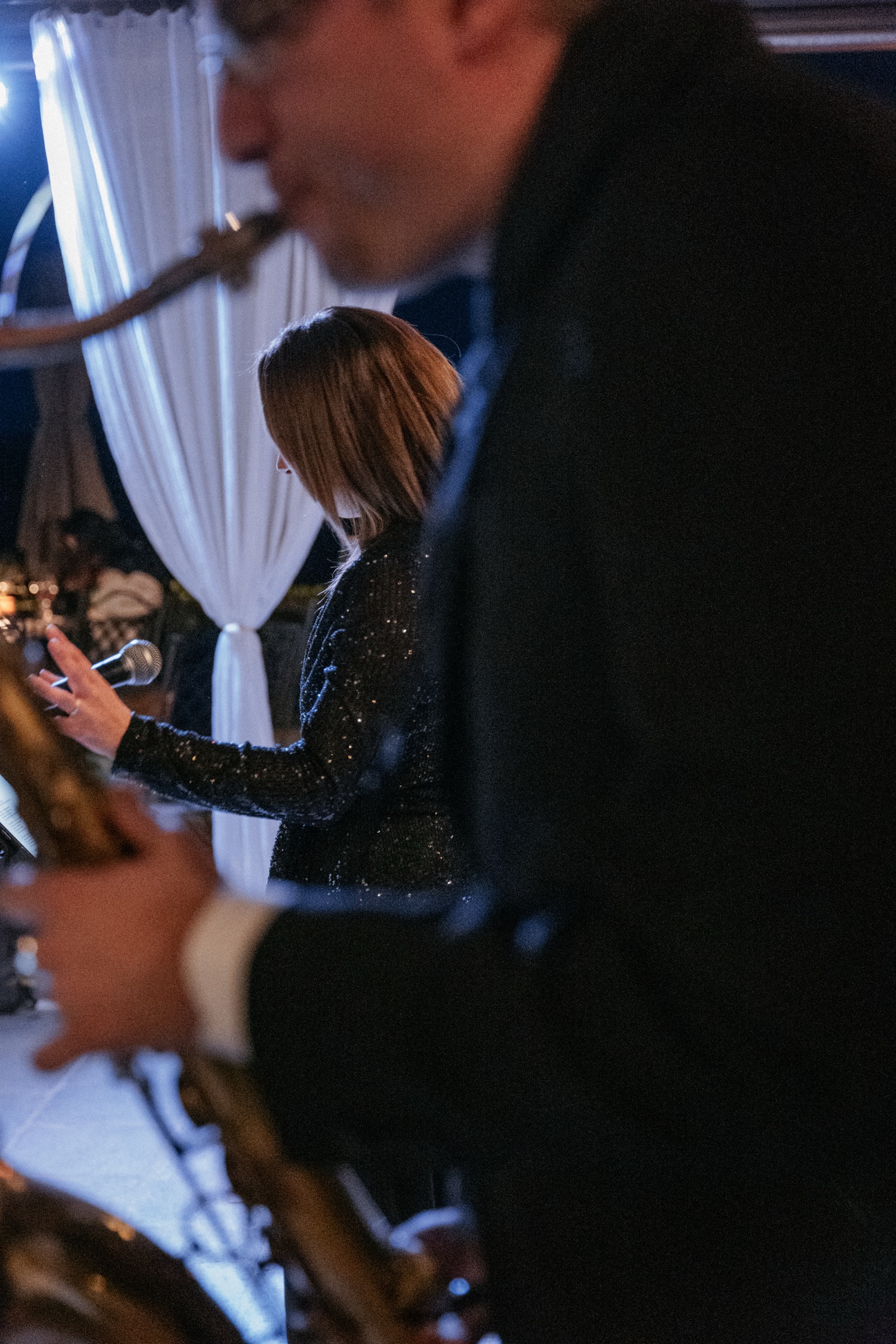 Saxophonist in the foreground and vocalist in a sequined dress behind a white curtain at a wedding in Tuscany